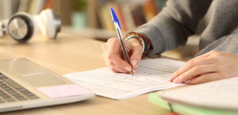 Close up of a student holding a pen, filling out a scholarship application